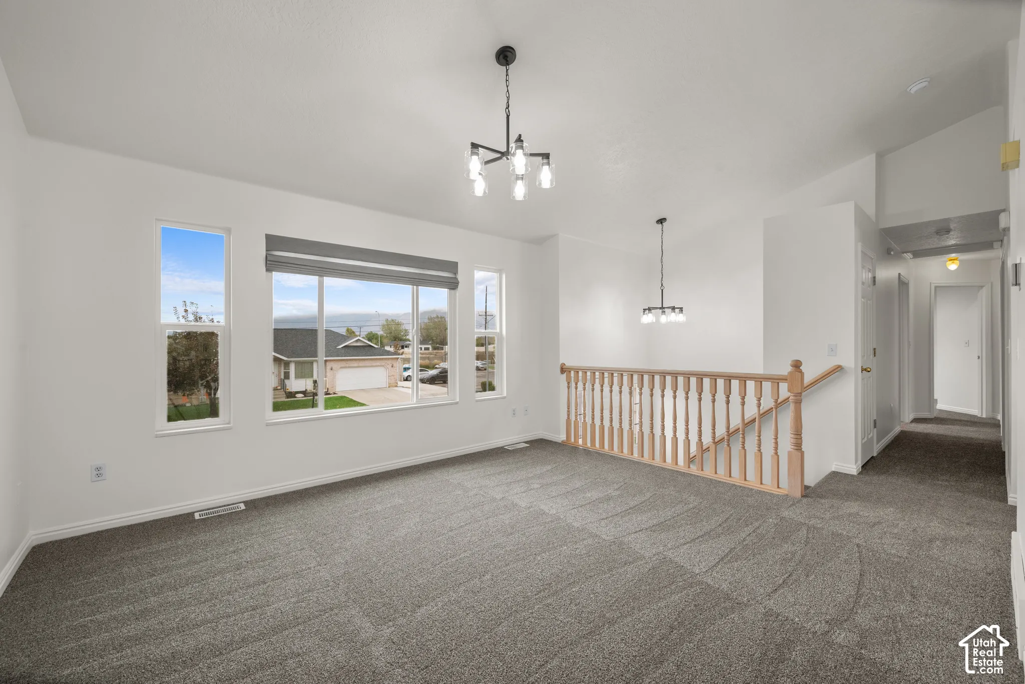 Vaulted ceilings with multi-arm chandeliers, neutral carpeting, and a wood-railing staircase