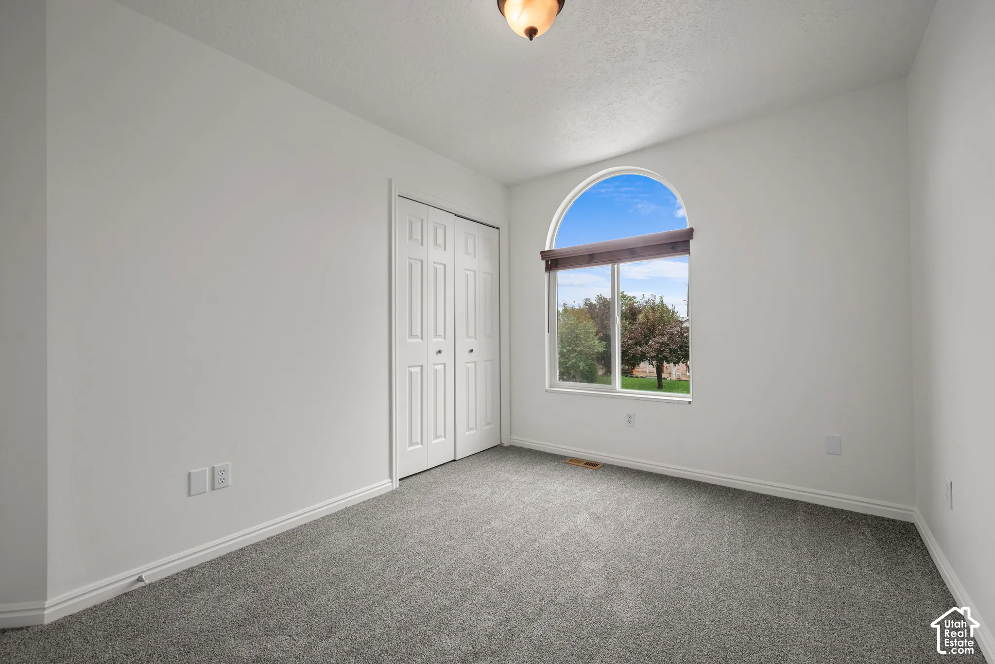 Room featuring arched window, dual-panel closet doors, wall-to-wall carpeting, and neutral paint palette