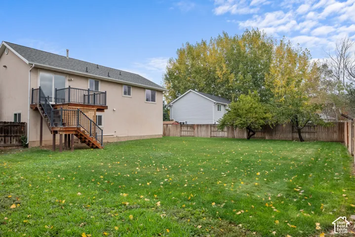 Expansive backyard featuring a large grass lawn, perimeter wood fencing, and elevated rear deck with metal railings
