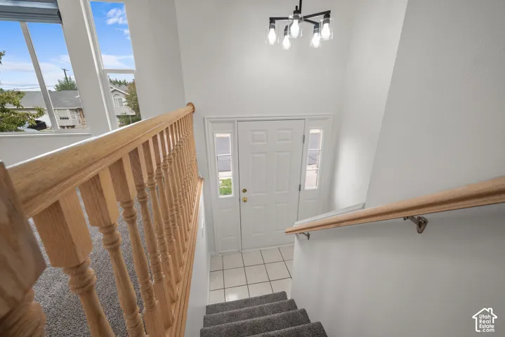 Entryway featuring a solid door with dual sidelights, tile flooring, high ceilings, a multi-light chandelier, and a wood-finish staircase railing
