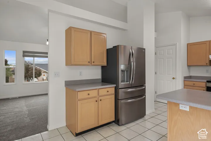 Kitchen featuring light wood-finish cabinetry, solid-surface countertops, stainless steel refrigerator, and tiled flooring