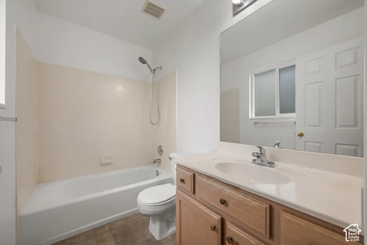 Bathroom featuring a wood-finish vanity with a molded countertop, a large wall-mounted mirror, a porcelain bathtub-shower combination with surround panels, and tile flooring