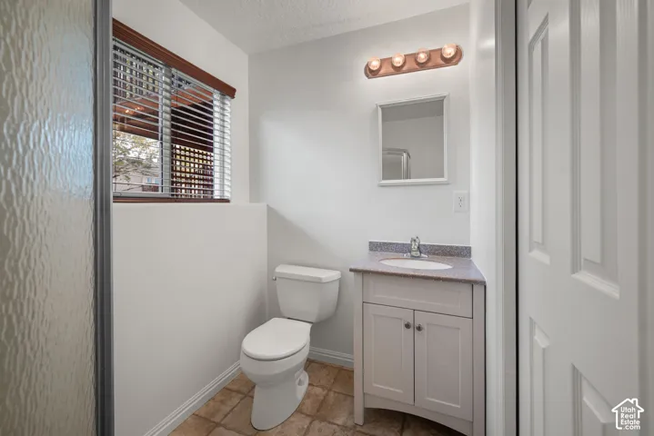 Bathroom featuring a vanity with a solid-surface countertop, an integrated sink, a multi-bulb light fixture, a framed wall mirror, and tile flooring