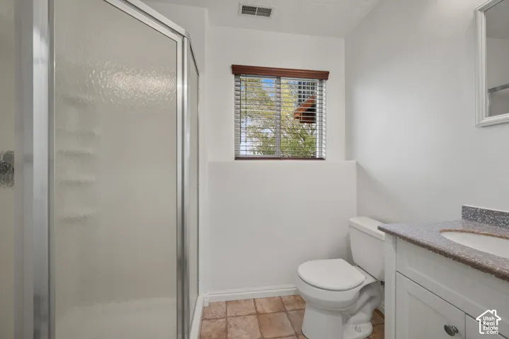 Bathroom featuring a walk-in shower with metal-framed glass doors, a vanity with stone-finish countertop and integrated sink, and ceramic tile flooring