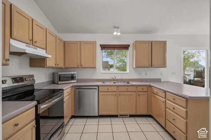 Kitchen featuring wood cabinetry, stainless steel appliances, solid-surface countertops, dual-basin sink, and ceramic tile flooring
