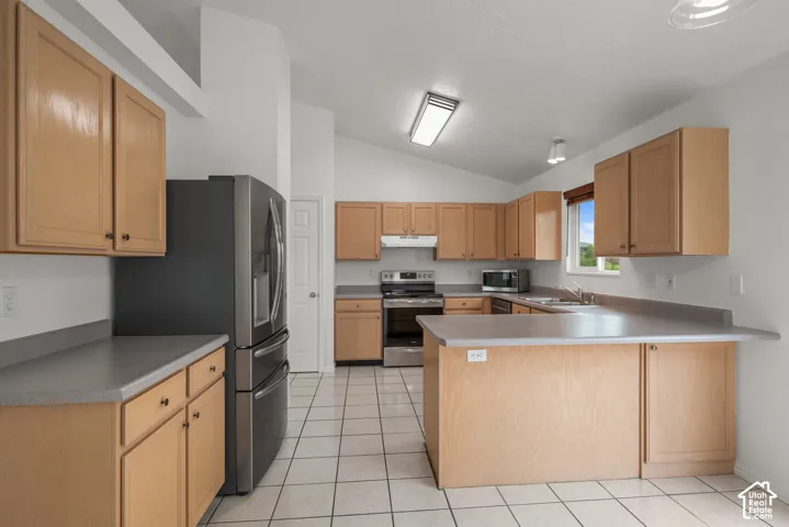 Kitchen featuring natural wood cabinetry, stainless steel appliances, solid-surface countertops, tile flooring, and vaulted ceilings