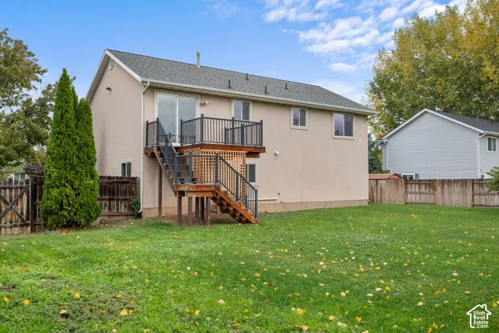 Rear exterior featuring a stucco facade, an elevated deck with metal railings, a staircase, and a fenced backyard