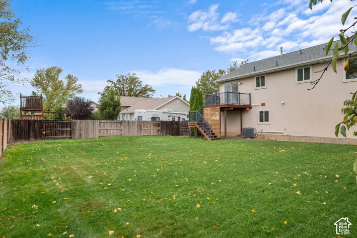 Expansive backyard featuring a level lawn, a raised wooden deck with metal railing, a staircase providing ground-level access, and full perimeter wood fencing