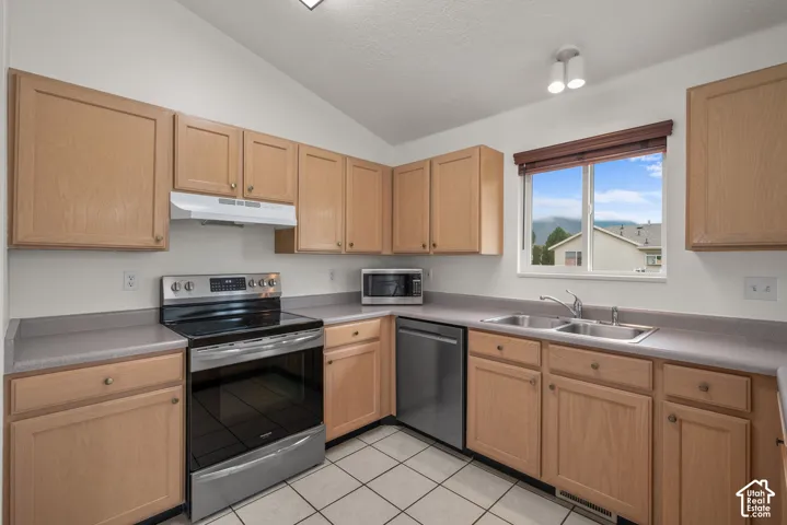Kitchen featuring natural-finish wood cabinetry, solid-surface countertops, stainless steel appliances, tile flooring, and a double-basin sink