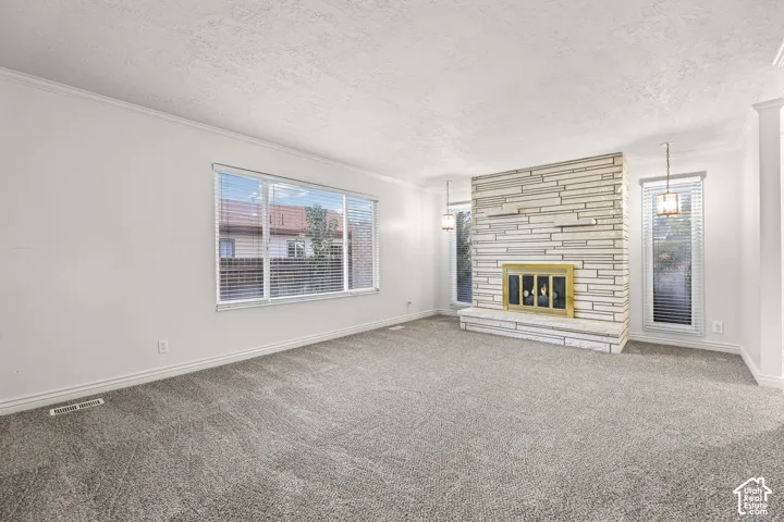 Floor-to-ceiling stone fireplace with an elevated hearth, wall-to-wall carpeting, multiple windows, and dual pendant lighting fixtures