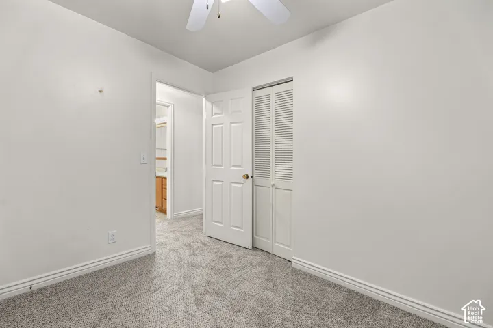 Room featuring neutral wall-to-wall carpeting, a multi-panel interior door, a louvered bifold closet door, and a ceiling fan