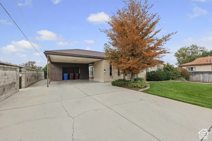 Brick exterior featuring a covered carport, concrete driveway, and a maintained lawn
