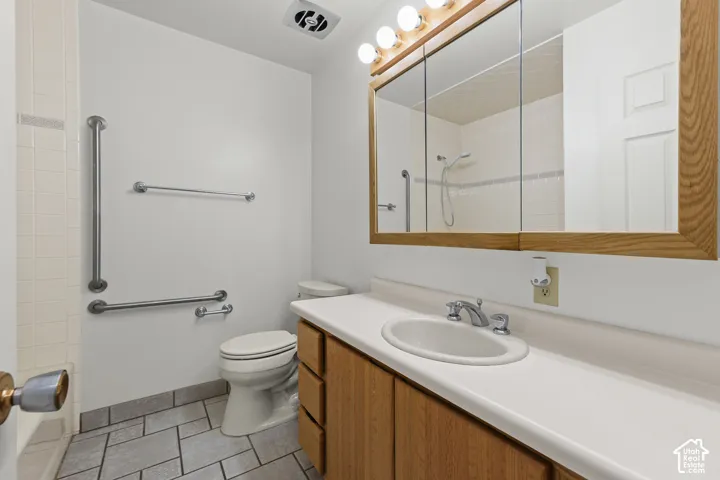 Bathroom featuring a vanity with wood-finish cabinetry, a white integrated sink, a multi-panel medicine cabinet, tiled flooring, and chrome grab bars