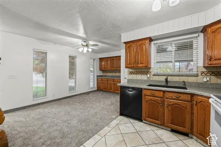 Kitchen featuring wood cabinetry, stone-finish countertops, tile flooring, and integrated black dishwasher
