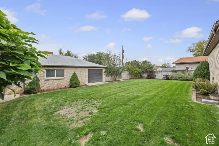 Expansive backyard featuring a manicured lawn, perimeter fencing, brick-exterior detached garage, and mature landscaping
