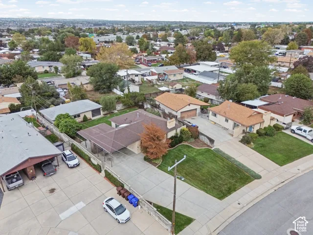 Aerial perspective of a property featuring an attached carport, expansive concrete driveway, masonry retaining wall, and a manicured front lawn