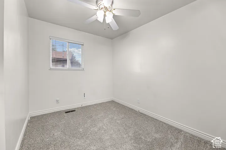 Neutral-toned wall-to-wall carpeting, white walls, sliding window, and ceiling-mounted light fixture with a central fan