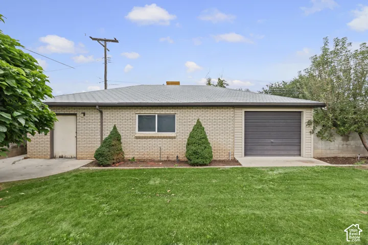 Single-story light-colored brick exterior featuring a low-pitch roof, attached garage with roll-up door, exterior access door, and concrete patio