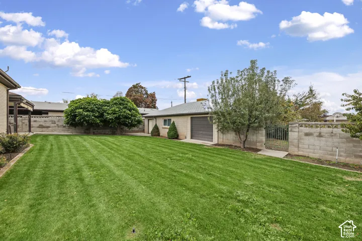 Expansive backyard featuring a manicured lawn, masonry perimeter walls, mature trees, and a detached single-car garage