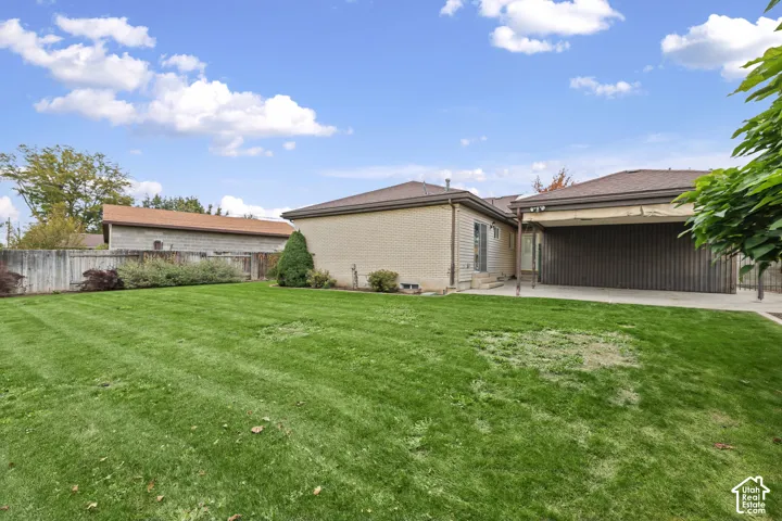 Expansive backyard featuring a manicured lawn, full-width concrete patio, covered outdoor area, and wood privacy fencing