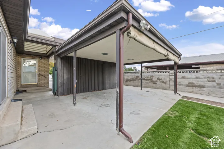Covered carport featuring a concrete parking pad, vertical siding, an attached retractable awning, and recessed lighting