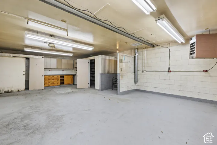 Expansive garage featuring concrete block walls, painted concrete flooring, built-in cabinetry, dual fluorescent lighting fixtures, and a wall-mounted heater unit