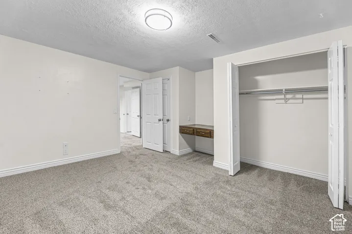 Room featuring neutral carpeting, a built-in wall-mounted desk with drawers, a walk-in closet with integrated shelving, and a flush-mount ceiling light fixture