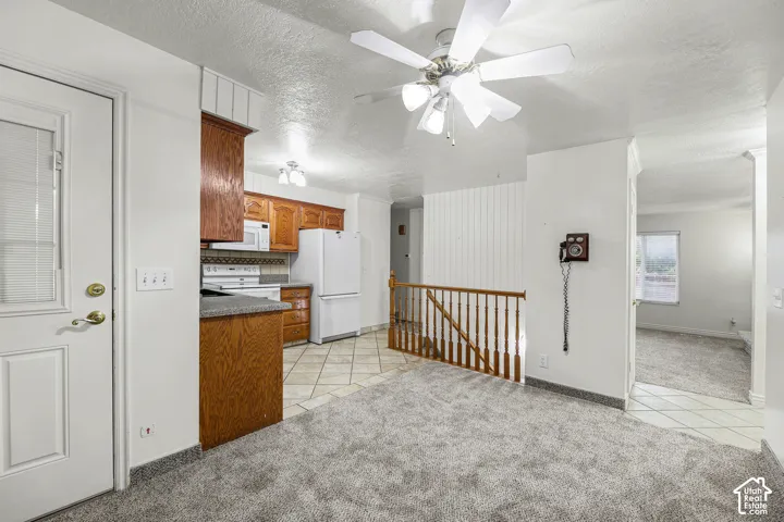 Kitchen area featuring wood cabinetry, solid surface countertops, tile flooring, and a ceiling fan with multi-light fixture, accompanied by wood-post staircase railing