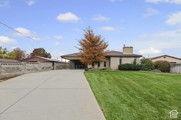 Single-story exterior featuring light-toned brick masonry, a spacious concrete driveway, a covered carport, and a prominent brick chimney