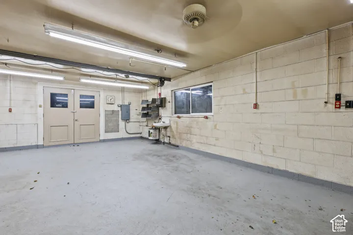 Garage space featuring concrete block walls, painted concrete flooring, wall-mounted utility sink, and dual overhead fluorescent lighting