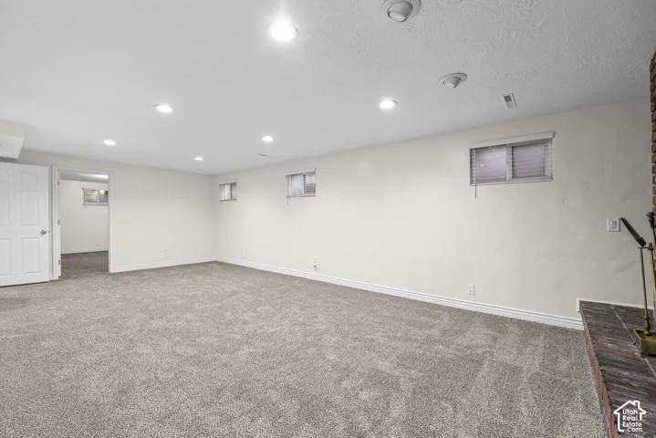 Neutral-toned carpeting, recessed ceiling lighting, textured wall finish, and brick fireplace hearth