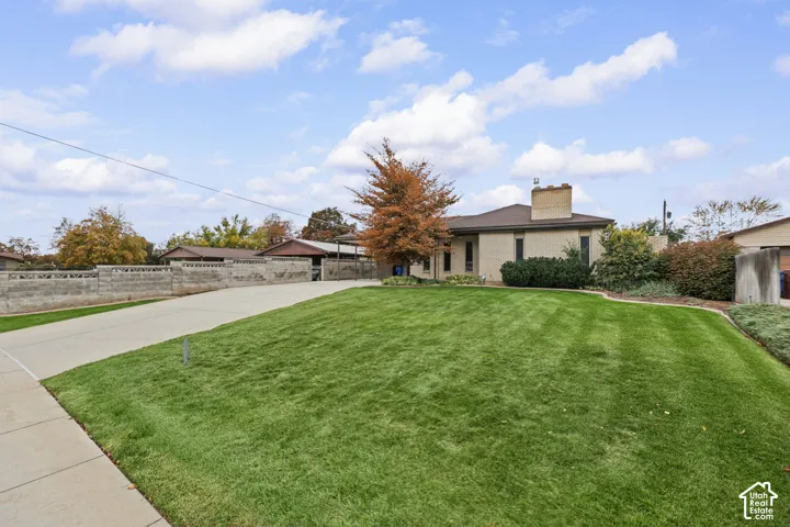 Single-level residence with a light-colored brick exterior, prominent chimney, expansive front lawn, concrete driveway, and decorative masonry perimeter wall
