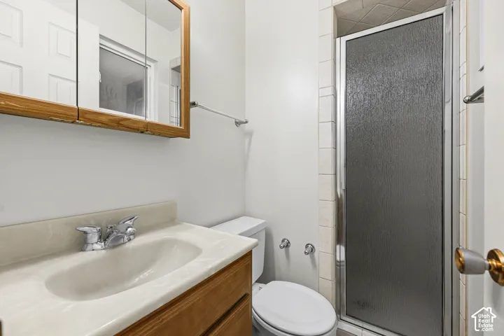 Bathroom featuring a wood-finish vanity with a molded basin, integrated countertop, medicine cabinet, and a tiled stall shower with a framed glass door