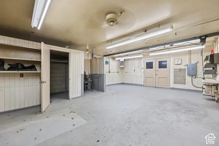 Garage interior featuring concrete flooring, built-in storage shelving, linear lighting fixtures, double doors, and a wall-mounted utility sink