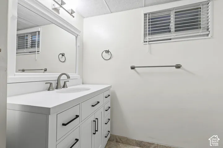 White vanity cabinet featuring a solid surface countertop with integrated sink, brushed-finish faucet, matte black hardware, and large wall-mounted mirror