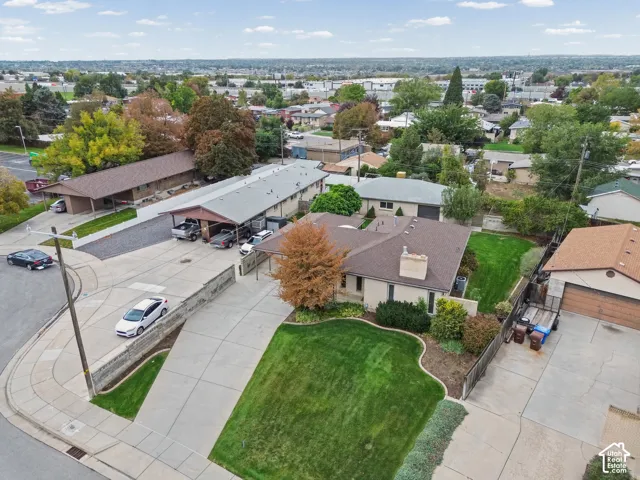 Aerial perspective featuring a single-story residence with a multi-car carport, expansive concrete driveway, masonry retaining walls, and manicured landscaping