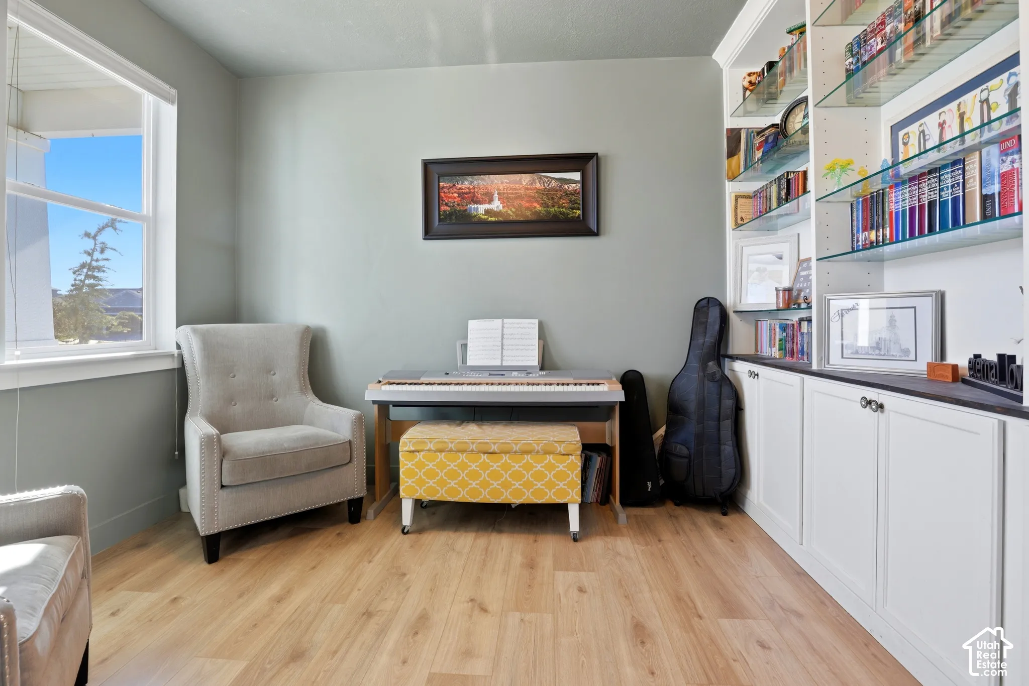 Built-in cabinetry featuring white lower cupboards, glass shelving, and a dark countertop, complemented by light-toned wood-finish flooring and a multi-pane window