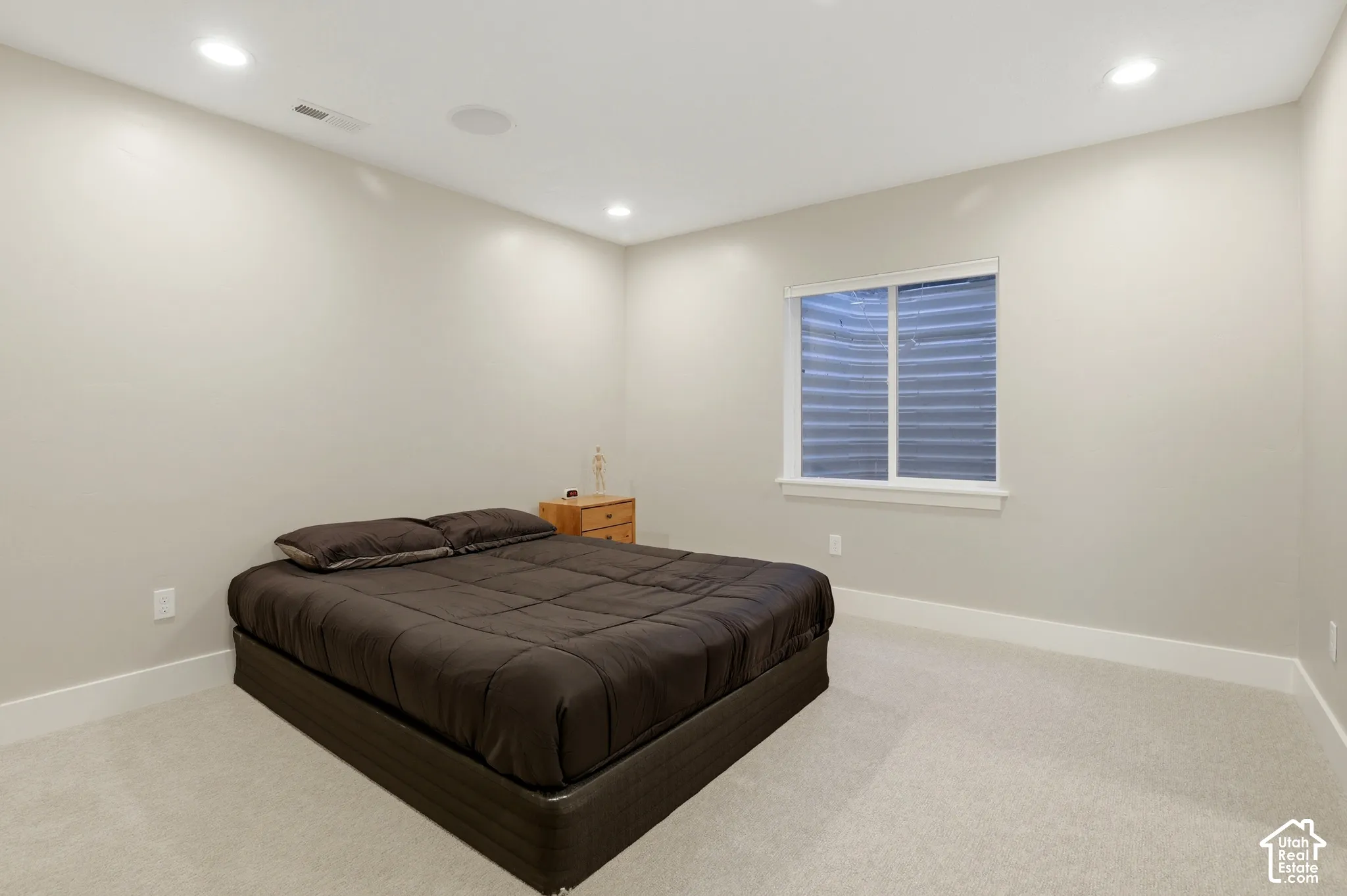 Neutral-toned interior space featuring recessed ceiling lighting, light-colored wall-to-wall carpeting, and a recessed window with a corrugated metal window well