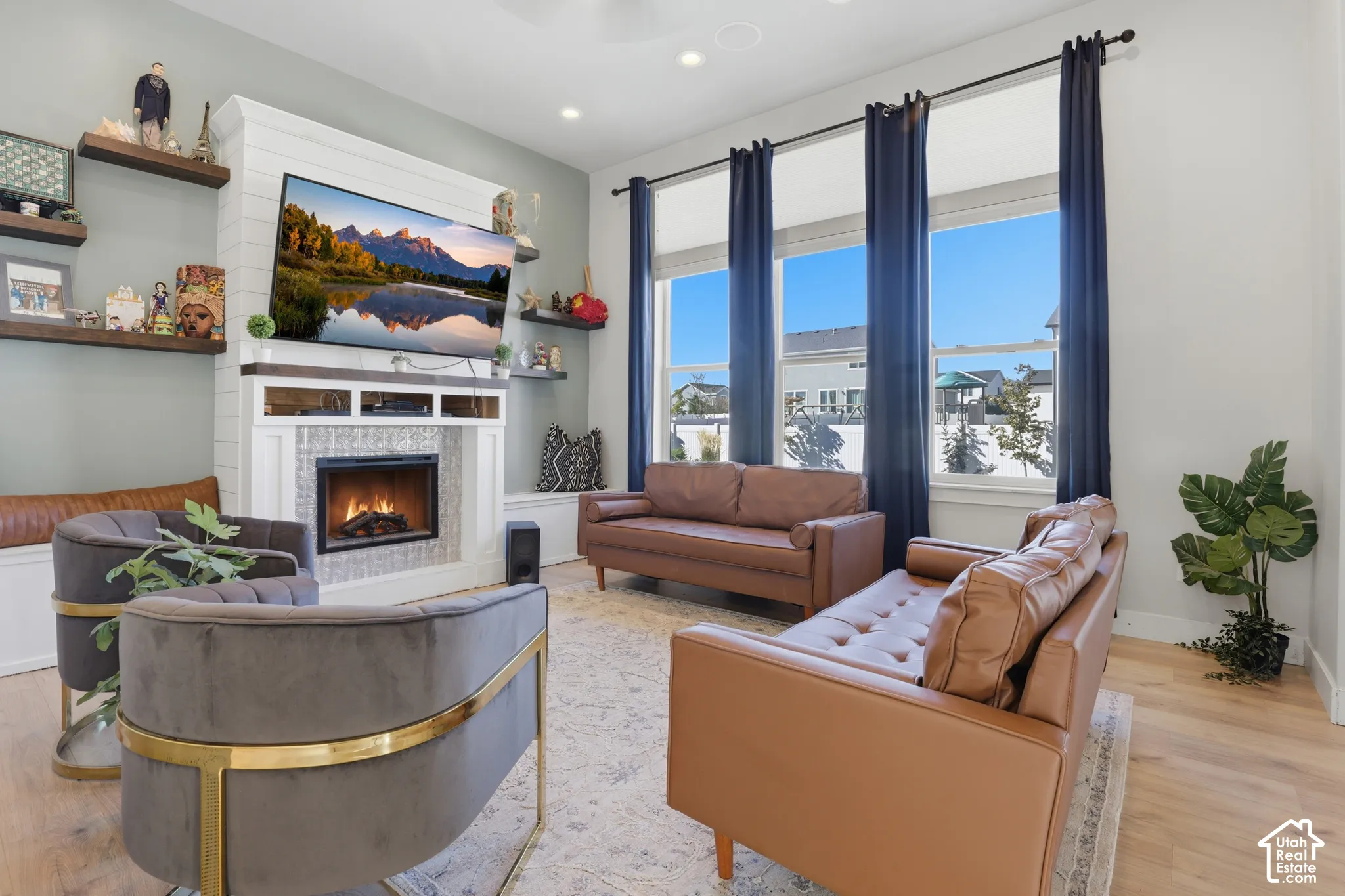 Living area featuring high ceilings, large multi-pane windows, a fireplace with a custom mantel and tile surround, horizontal board wall paneling, and wood-finish flooring