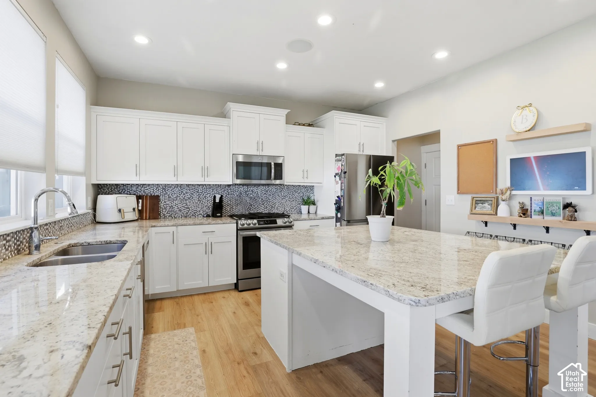Kitchen featuring white shaker cabinetry, stone countertops, a central island with integrated seating, stainless steel appliances, and a mosaic tile backsplash