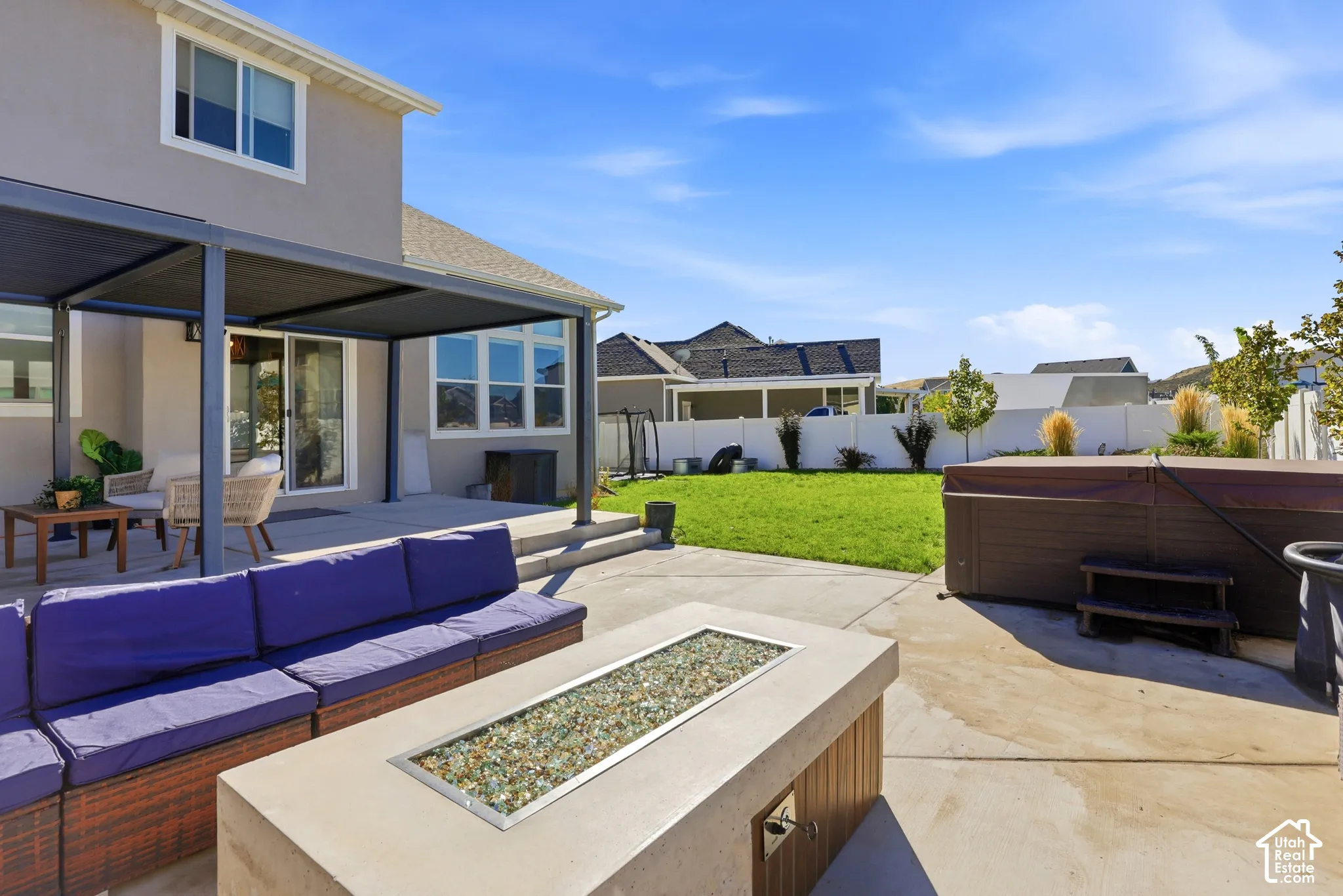 Backyard featuring a concrete patio, a covered pergola, a built-in fire pit with glass fire media, and a vinyl perimeter fence