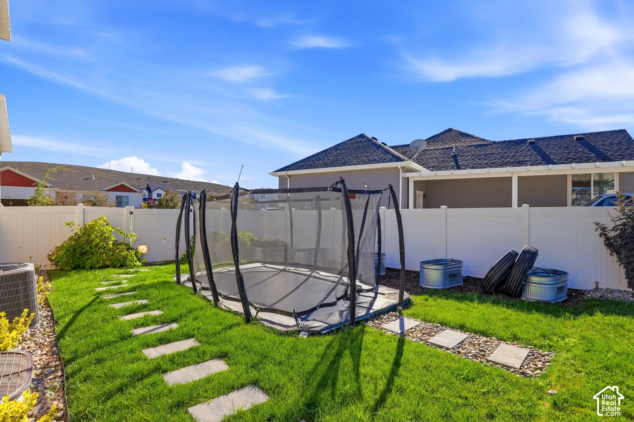 Fenced backyard featuring a manicured lawn, stone paver pathway, and covered patio area