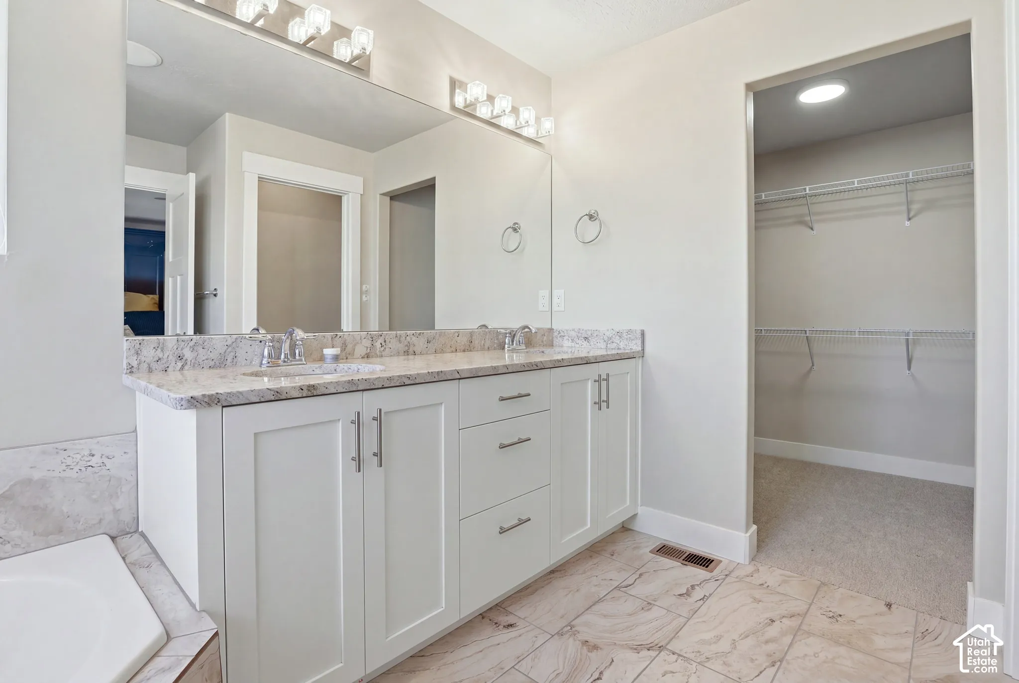 Bathroom featuring a dual-sink vanity with light stone countertop, Shaker-style cabinetry, a large wall-to-wall mirror, and multi-light fixtures
