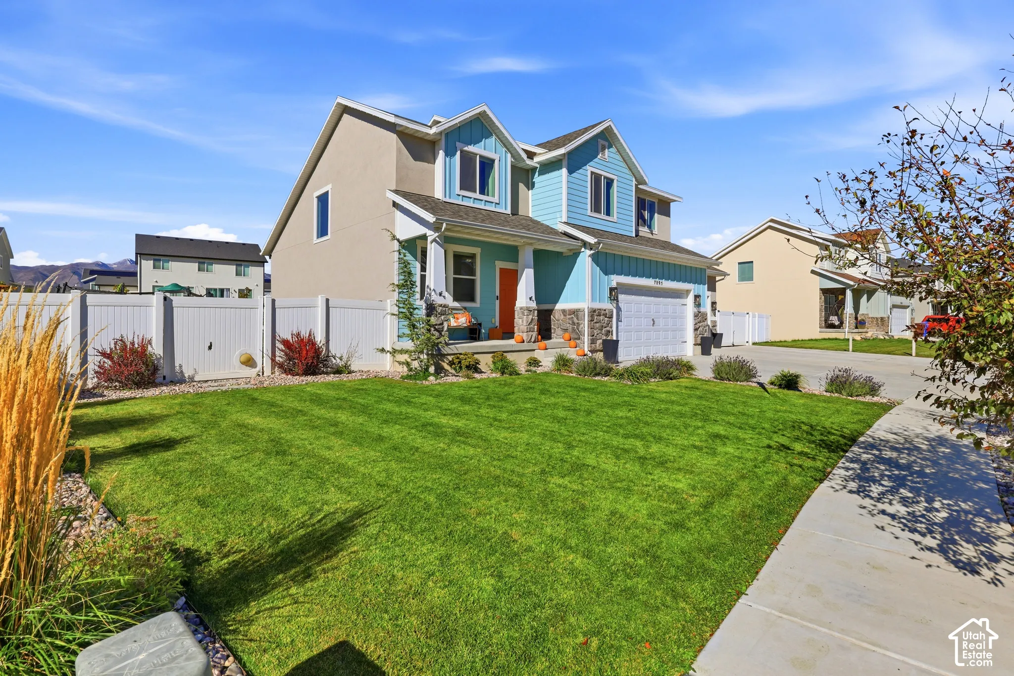 Two-story residence featuring a multi-textured exterior of stone veneer, horizontal siding, and board-and-batten accents, complemented by an attached two-car garage, a covered front entryway, and a perimeter vinyl fence