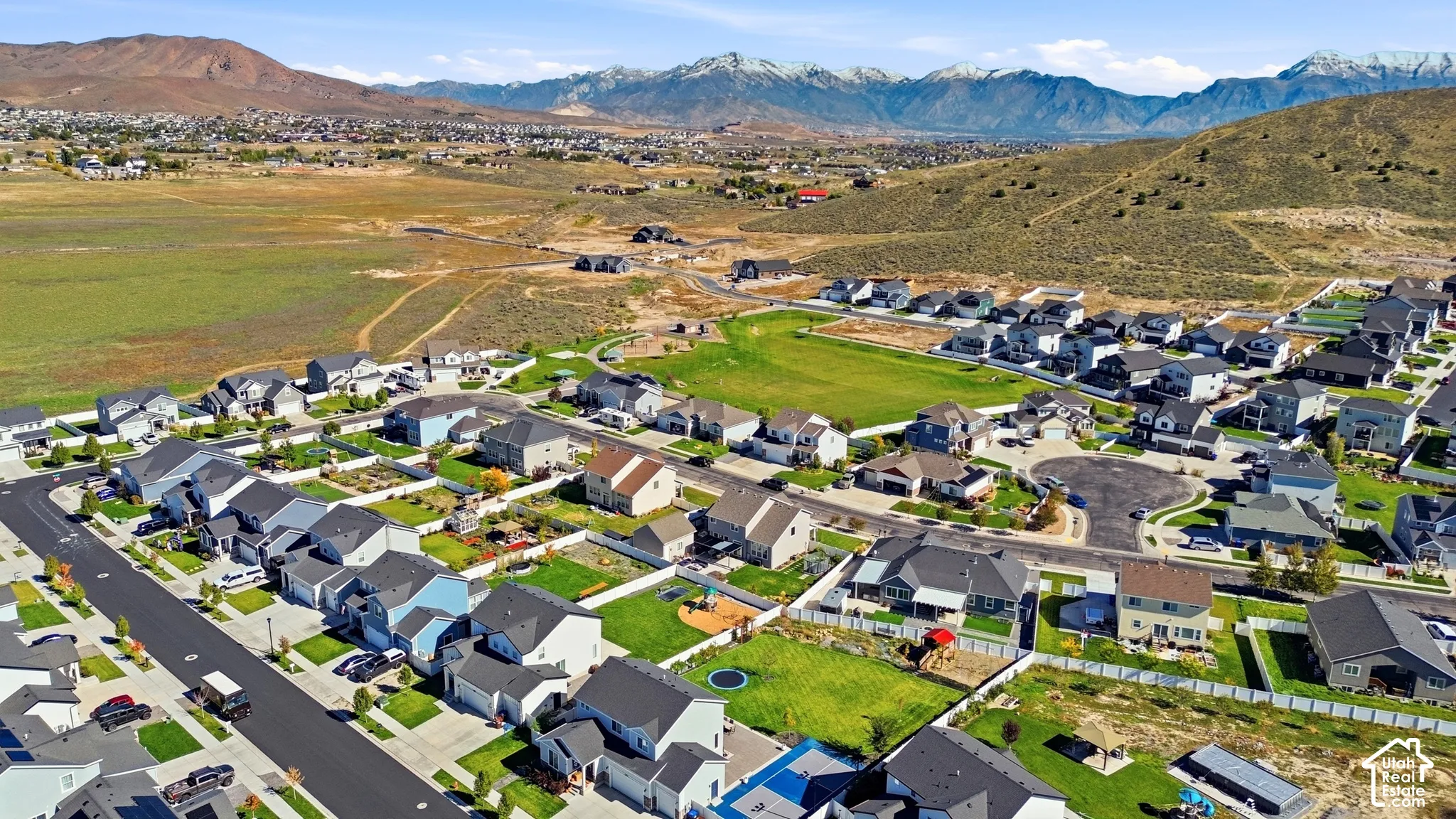 Aerial perspective of a suburban neighborhood featuring paved streets, single-family residential lots, manicured green space, and a mountainous horizon