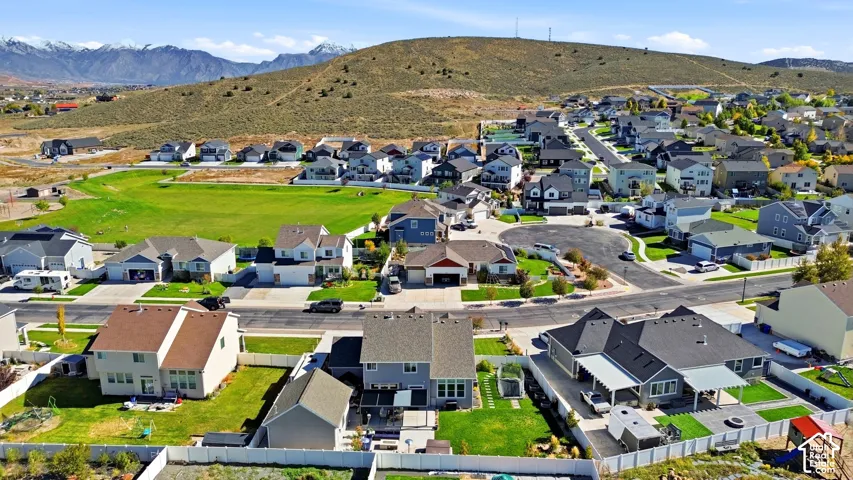 Aerial perspective featuring residential lots, paved streets, maintained lawns, perimeter fencing, and a mountain backdrop
