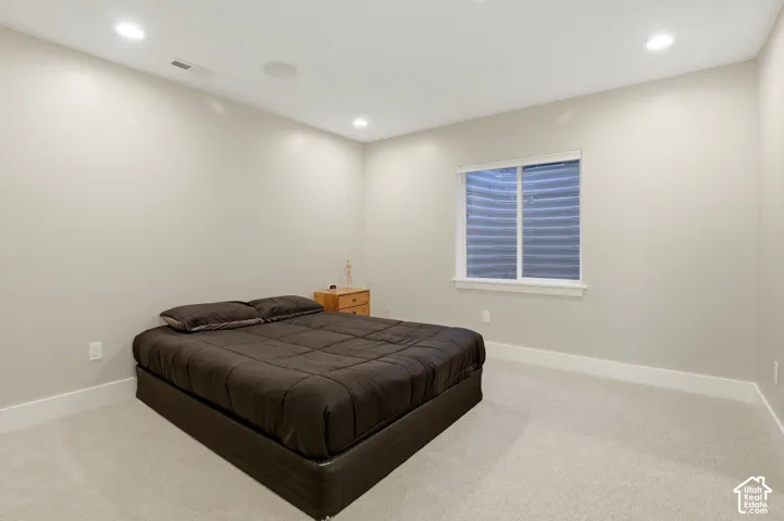 Neutral-toned interior space featuring recessed ceiling lighting, light-colored wall-to-wall carpeting, and a recessed window with a corrugated metal window well