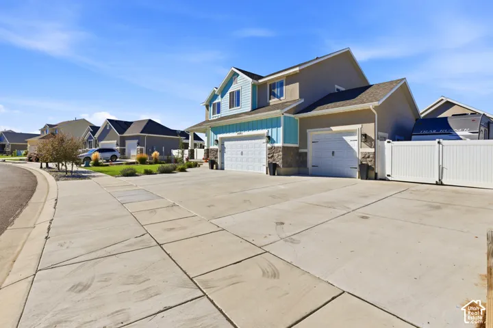 Multi-level exterior featuring vertical siding, stone veneer accents, a three-car garage, and a white vinyl privacy fence