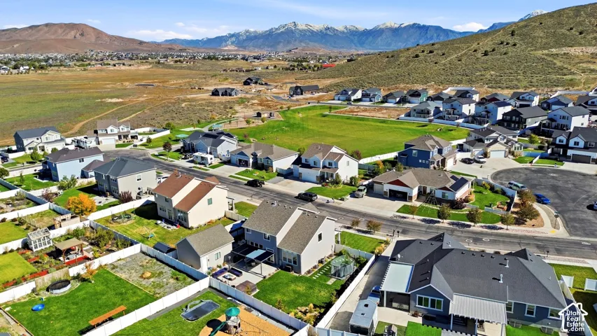 Aerial perspective of a suburban neighborhood featuring mountain backdrops, paved streets, residential lots with perimeter fencing, and open green space