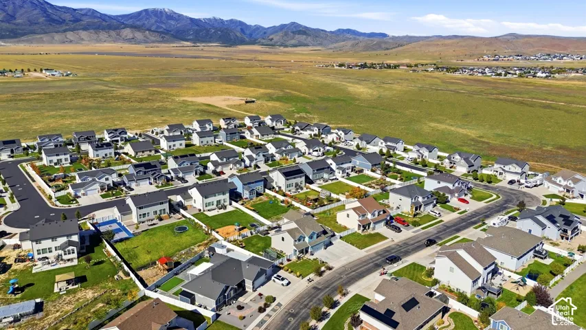 Aerial perspective of a suburban neighborhood featuring paved streets, multi-level residential homes, manicured lawn lots, and a backdrop of expansive mountain ranges